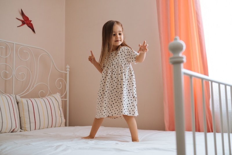 Happy little girl in motion jumping on a bed in a bedroom after waking up.