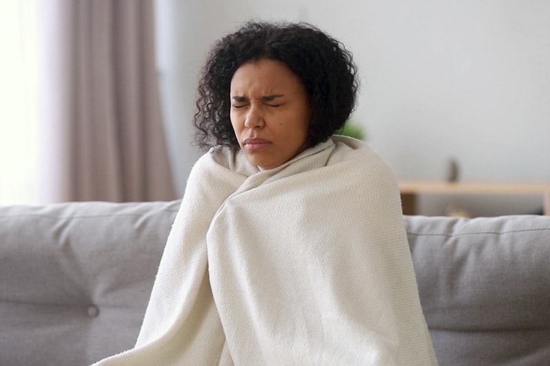 Upgrade Your Furnace. A woman sitting wrapped in a blanket in her cold home.